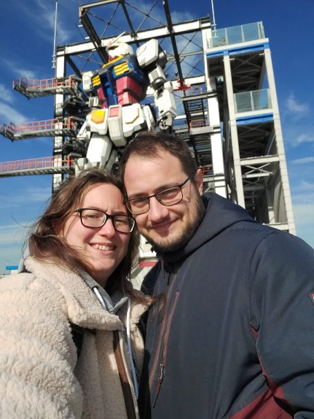 Pareja sonriente con una estatua de robot detrás en un día soleado.